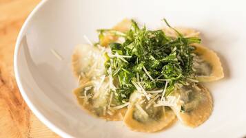 Une assiette blanche contenant des raviolis, recouverts de fromage râpé et de verdure.