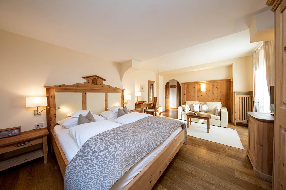 A spacious bedroom with a large bed, wooden headboard, bedside tables, and a desk with a chair.