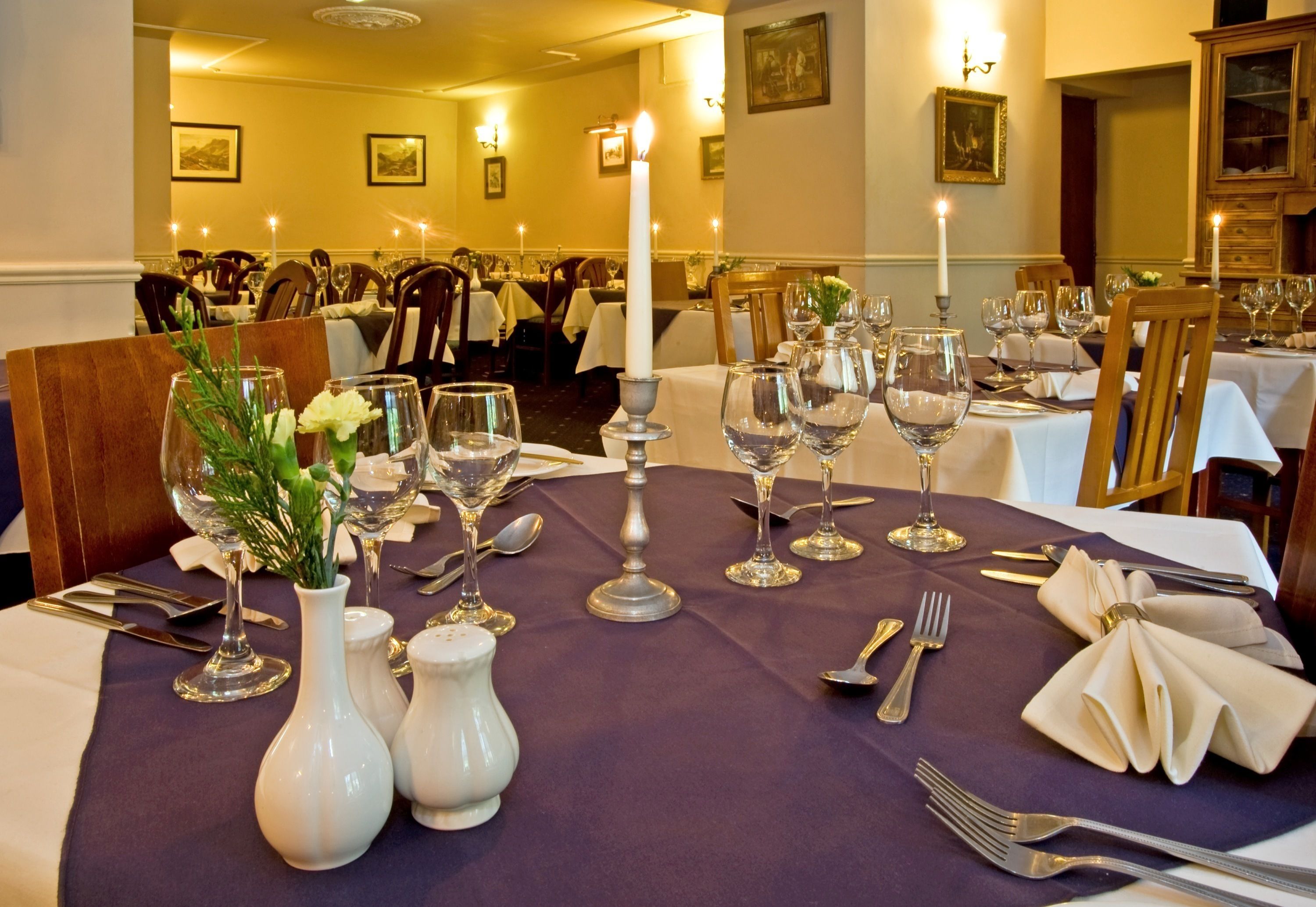 Una mesa de comedor dispuesta con mantel blanco, velas y cristalería.