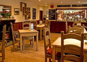 A cozy restaurant interior with wooden tables and chairs, a bar area with various bottles, and a menu board on the wall.