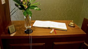 A wooden reception desk with a book, a telephone, and a vase of flowers.
