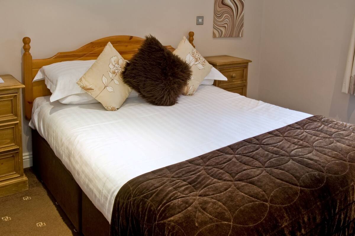 A neatly made bed with a brown quilt and white linens, flanked by wooden nightstands and a wooden headboard.