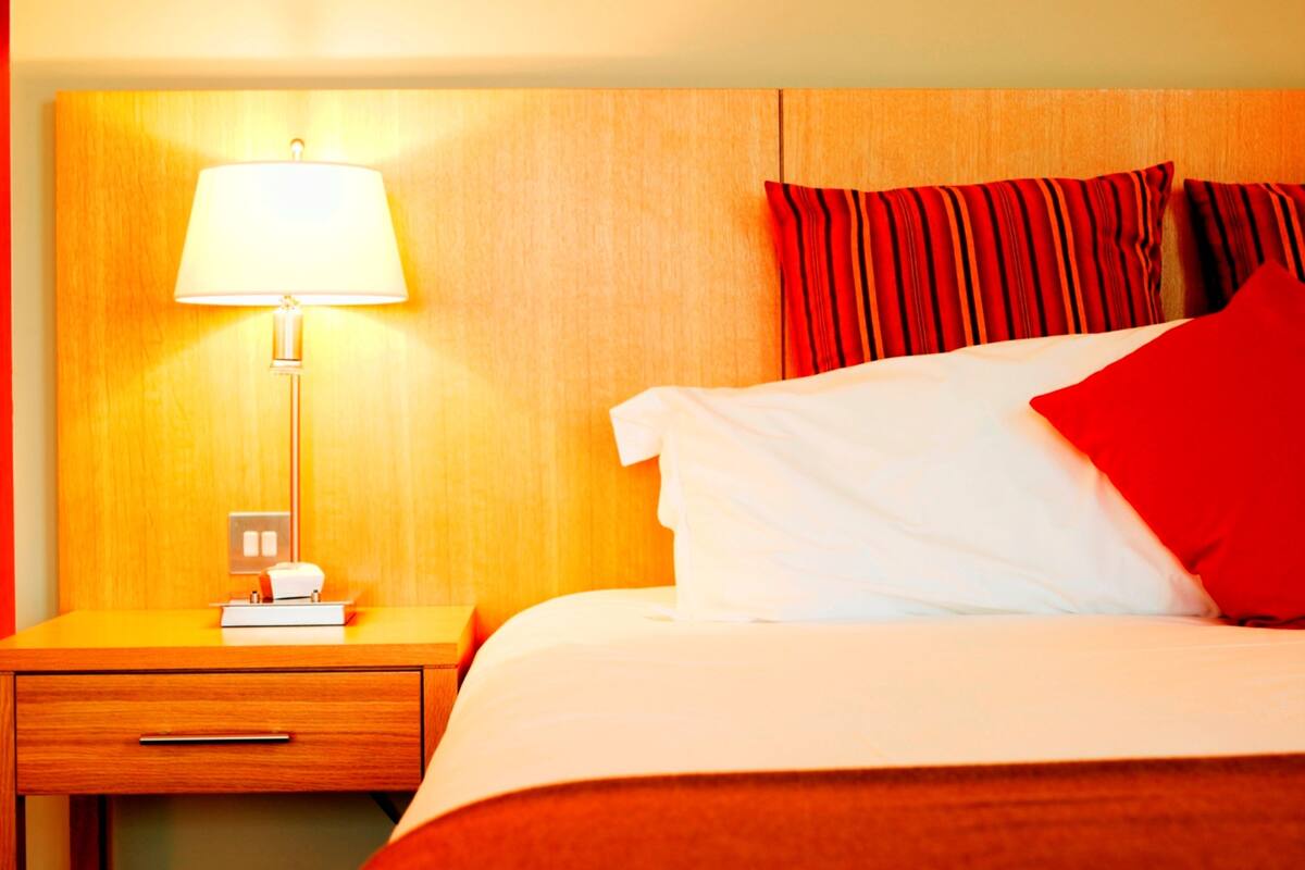 A hotel room with a bed, a nightstand, a lamp, and a red-striped curtain.
