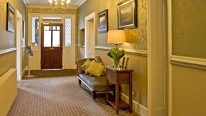 A hallway with patterned carpet, a sofa with cushions, a table with a lamp, framed pictures on the wall, and a door at the end. - New Dungeon Ghyll Hotel (Ambleside)