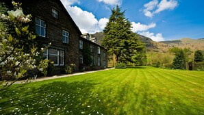 A stone building with multiple windows, a well-maintained lawn, and a large tree in the background. - New Dungeon Ghyll Hotel (Ambleside)