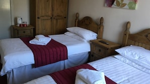 Een hotelkamer met twee bedden, houten hoofdeinden, een kledingkast, een nachtkastje met een lamp en een schilderij aan de muur.