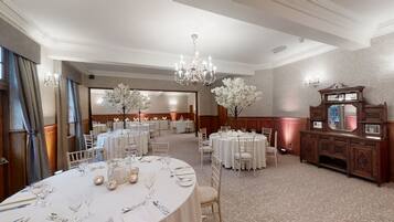 Une salle à manger élégante, avec des tables rondes, des nappes blanches et des lustres.