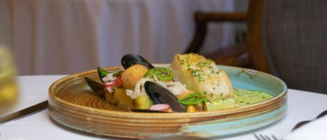 A plate of seafood with mussels, a piece of fish, and a breaded item, served on a ceramic plate with a green sauce.