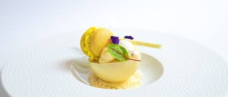 A dessert on a white textured plate with a yellow bowl, a scoop of ice cream, and a mint leaf garnish.