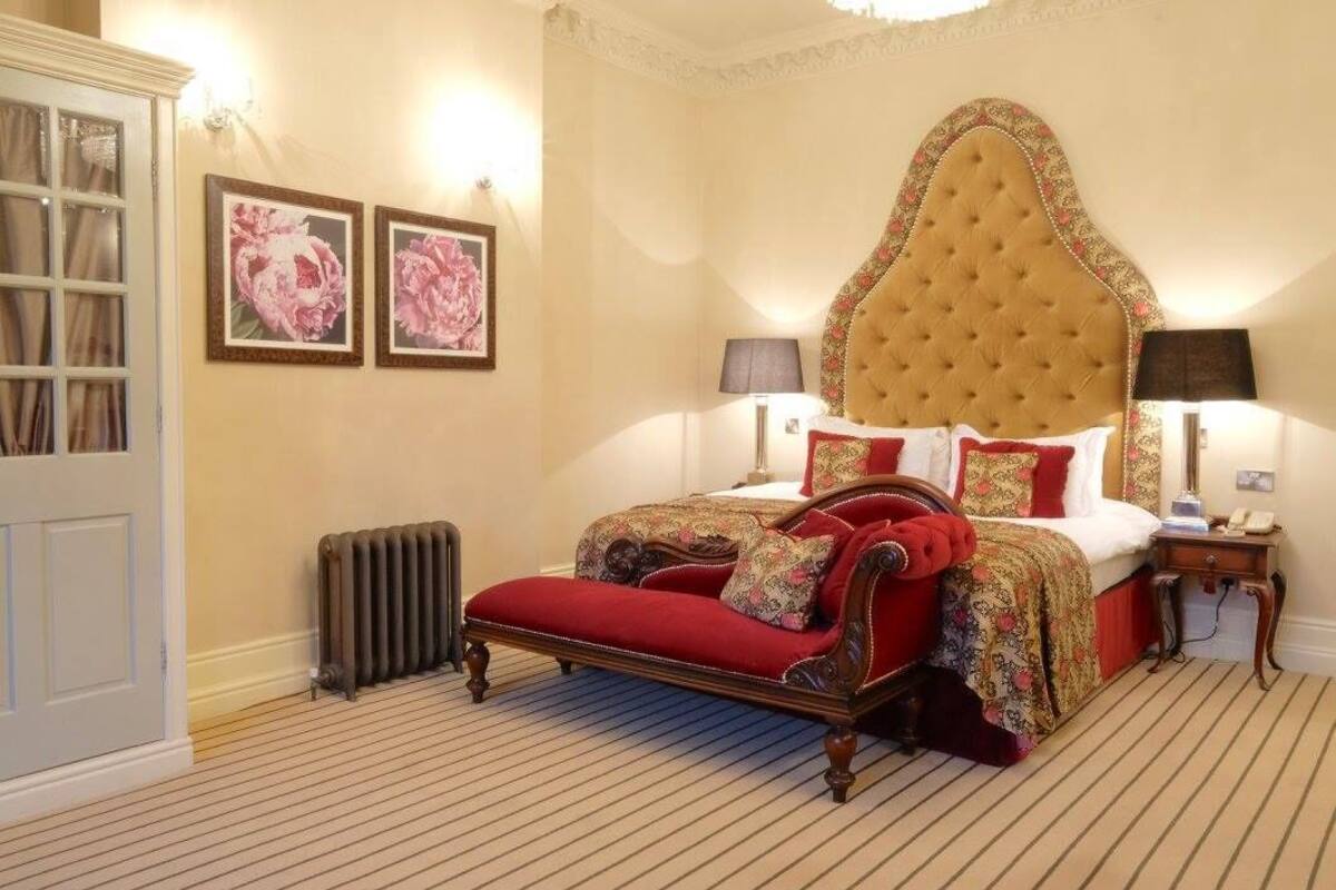 A bedroom with a large bed, a radiator, a nightstand, and two framed pictures on the wall.