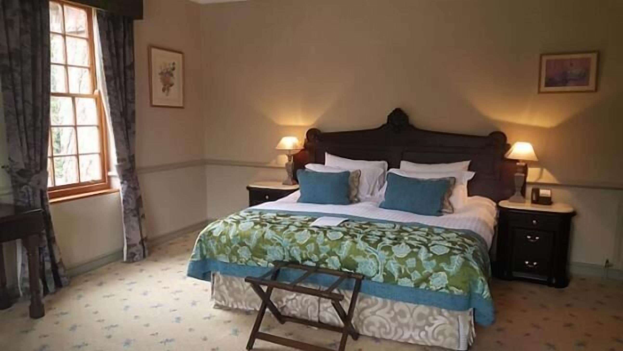 A neatly arranged bedroom with a large bed, two bedside tables with lamps, a window with curtains, and a small wooden chair.