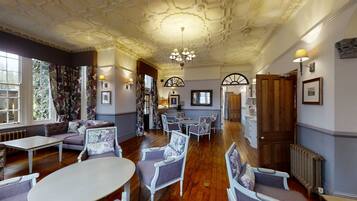 A room with a wooden floor, white furniture, and a chandelier. There are two windows with floral curtains and a door leading to another room.