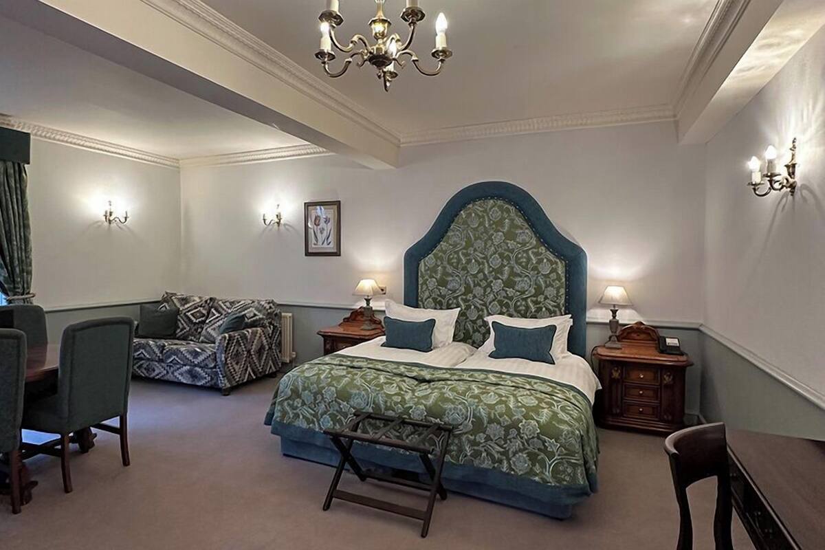 A bedroom with a large bed, a chair, a table, and a chandelier.