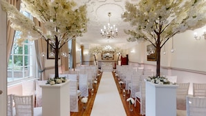 Un salón de bodas con un pasillo blanco, sillas a ambos lados y candelabros.