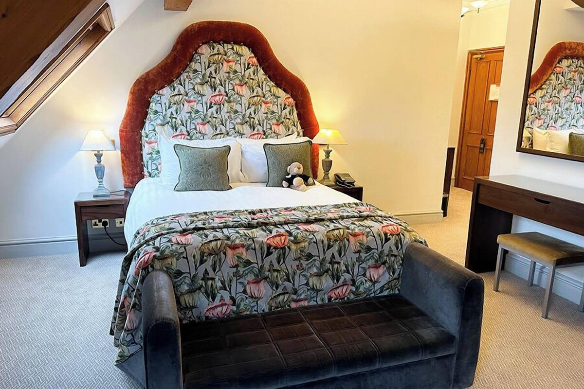 A bedroom with a floral bedspread, a tufted headboard, a bedside table with a lamp, and a bench.