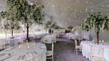 A banquet hall with round tables, white tablecloths, and chairs.