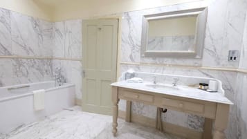 A bathroom with a marble floor, a bathtub, a vanity with a sink, and a mirror.