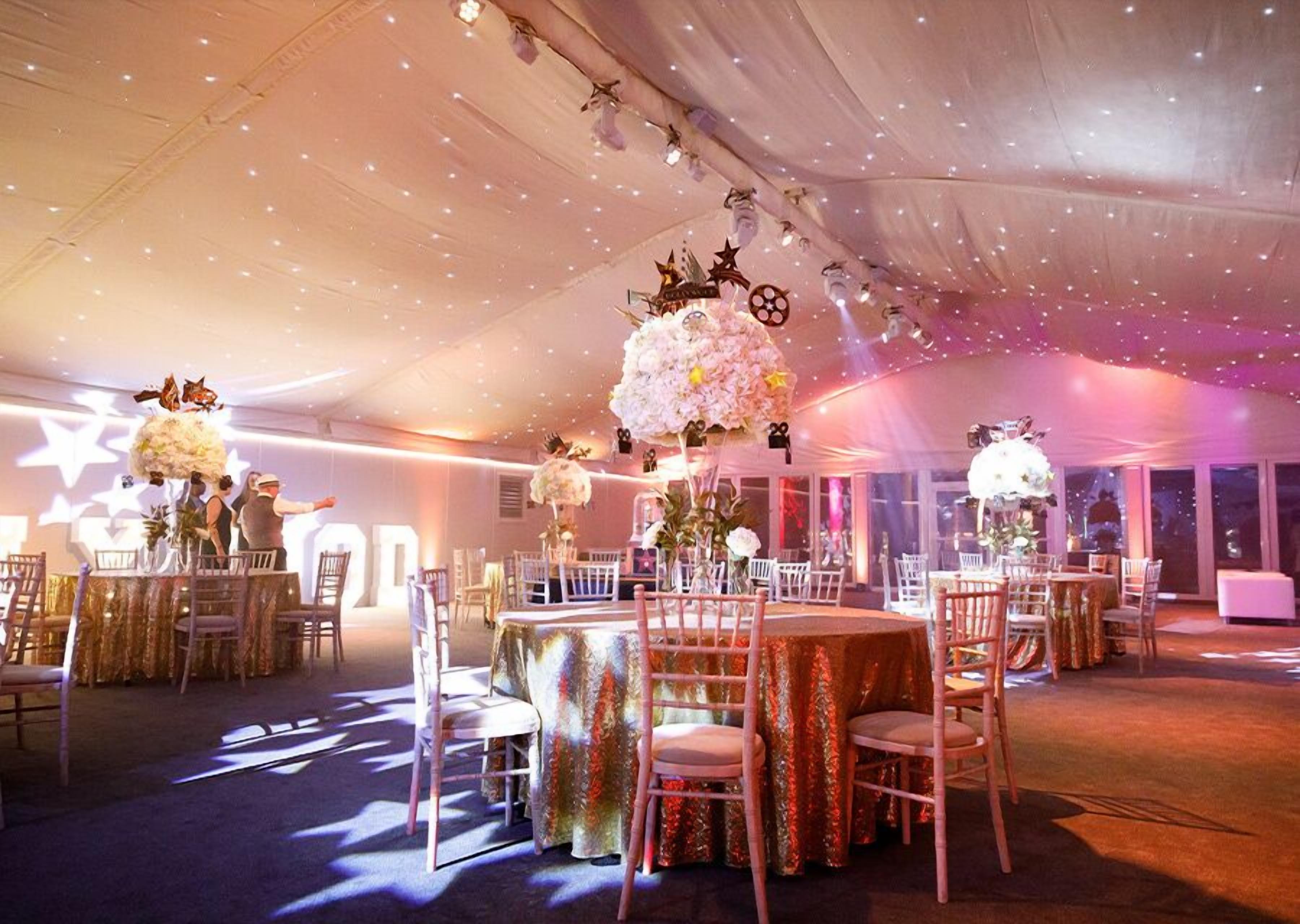 A tented event space with round tables and chairs, decorated with floral arrangements and star-shaped lights.