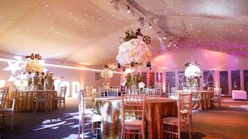 A tented event space with round tables and chairs, decorated with floral arrangements and star-shaped lights.
