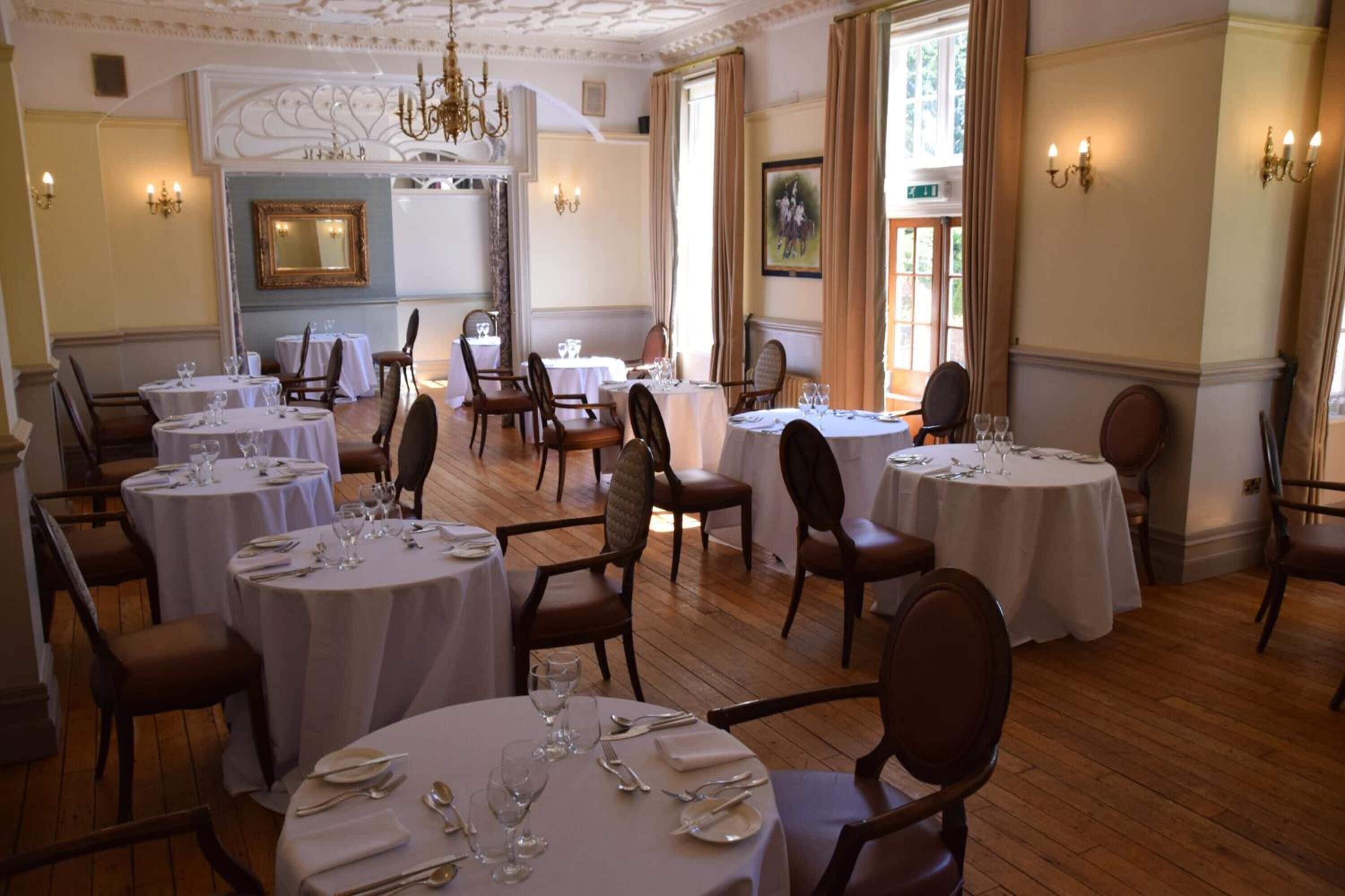 A dining area with round tables set for four, each with white tablecloths, chairs, and dinnerware.