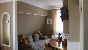 A living room with a sofa, two teddy bears, a television, and a small table with a lamp. - Teddybärenhotel (Kressbronn)
