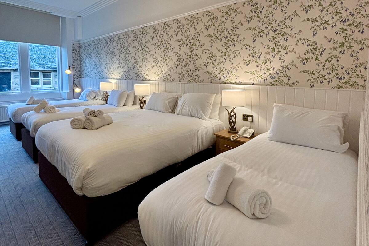 A hotel room with three beds, each with neatly folded towels, a bedside lamp, and a telephone.