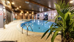 An indoor swimming pool with a tiled floor, surrounded by a wooden ceiling, and a potted plant in the foreground.