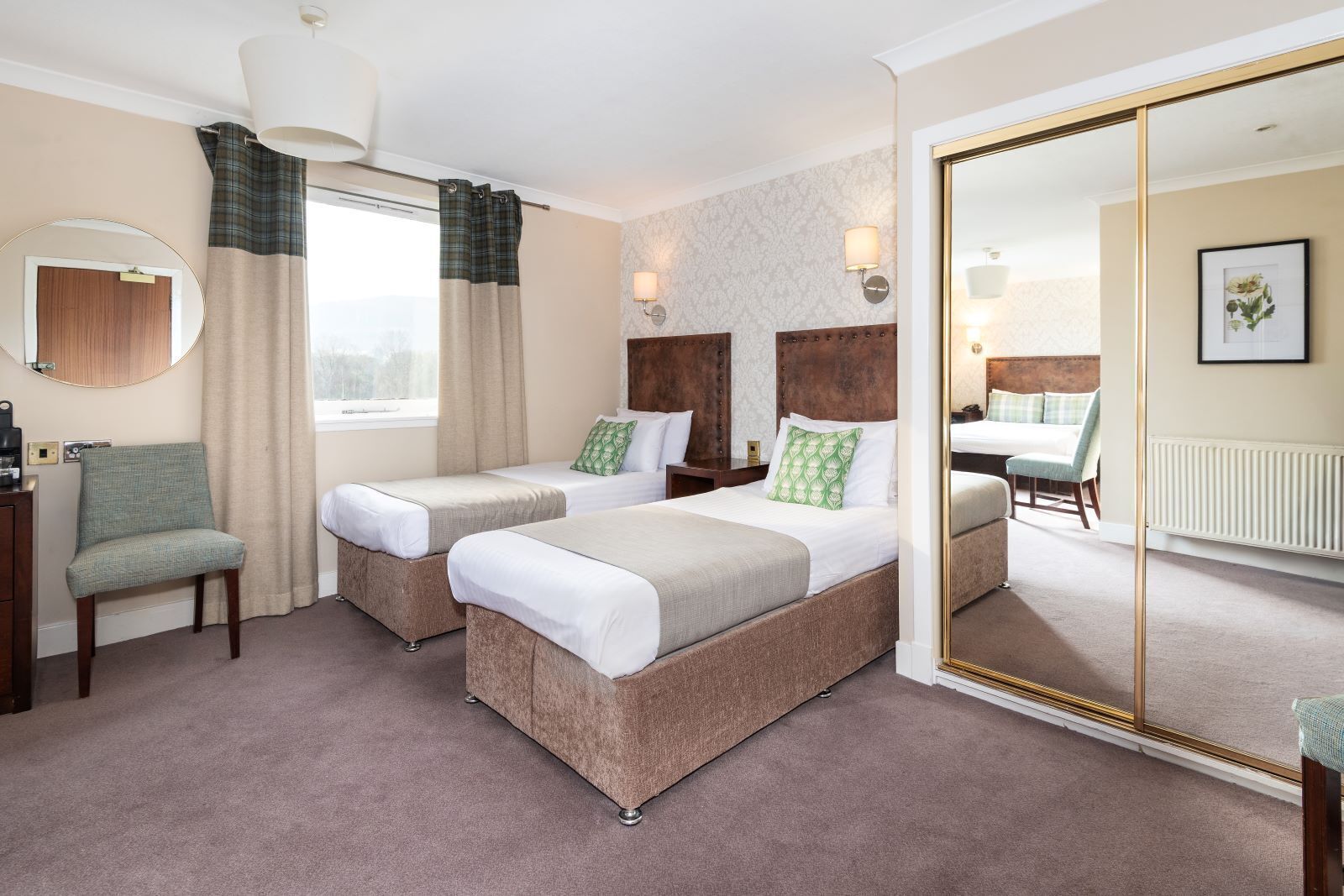 A hotel room with two beds, a sitting area, a mirror, and a view of the outside.