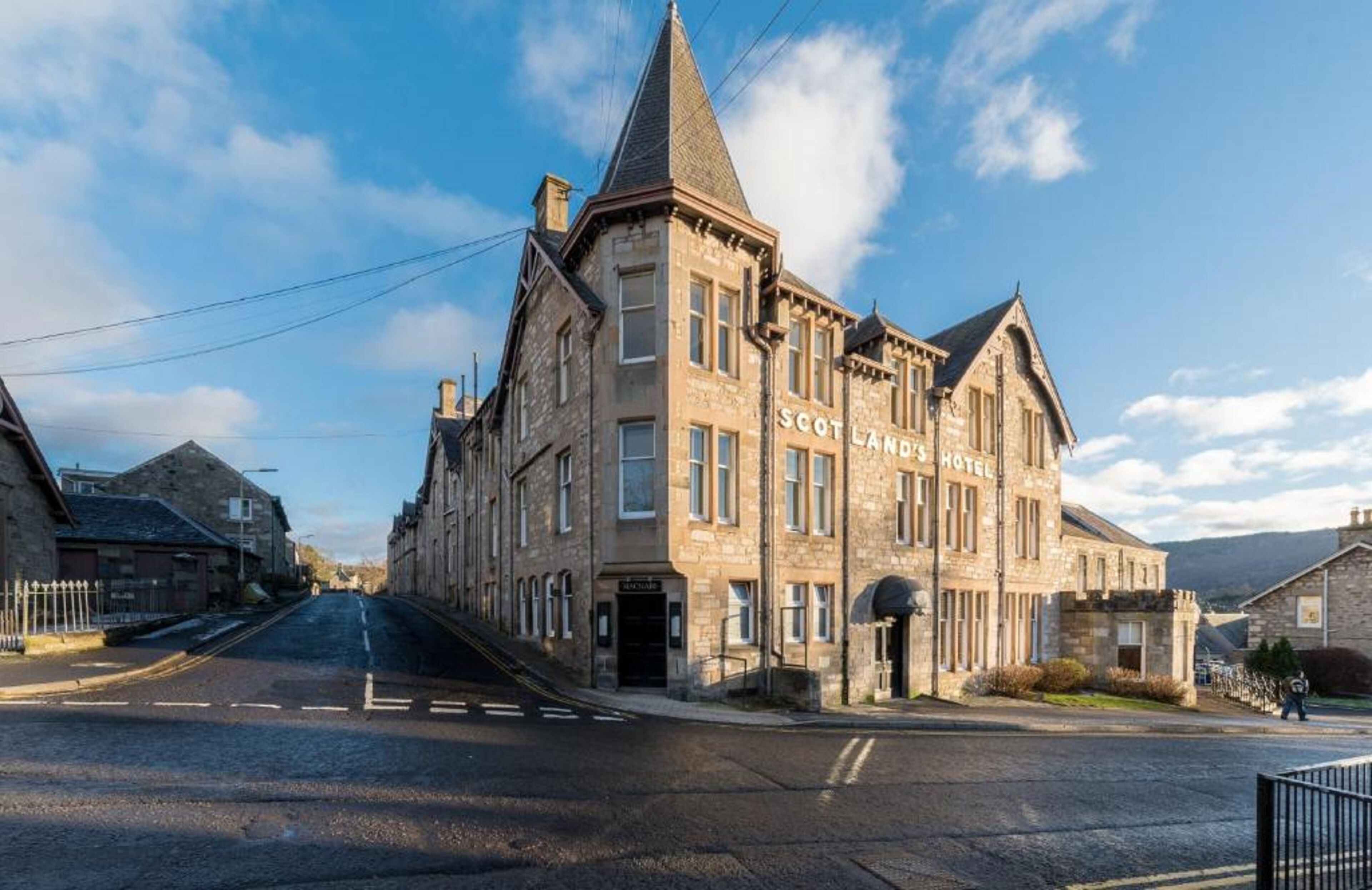 A historic stone building with a prominent tower, labeled "Scotland Hotel," featuring a traditional architectural style with multiple windows and a central entrance.