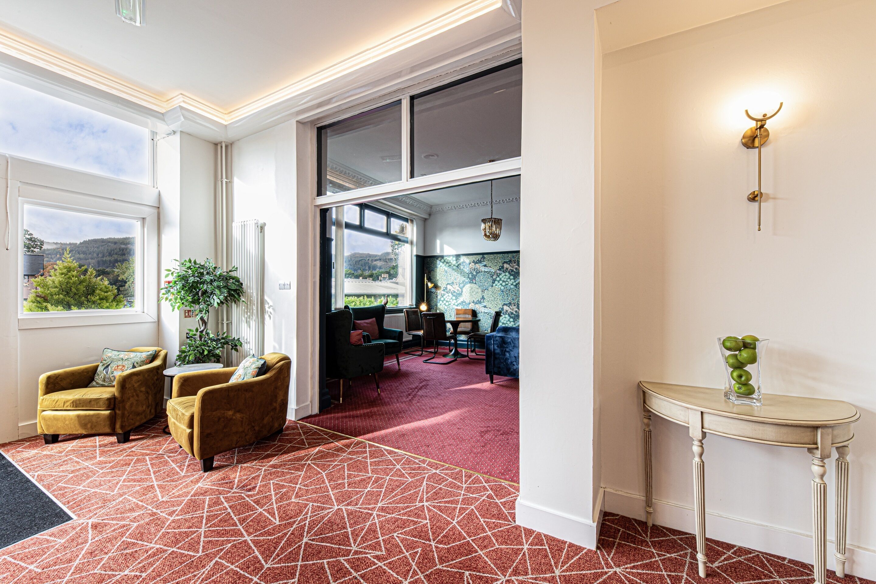 Een hotel lobby met een geometrisch patroon vloerkleed, een zithoek met banken en stoelen, een tafel met een vaas, en een uitzicht door grote ramen.