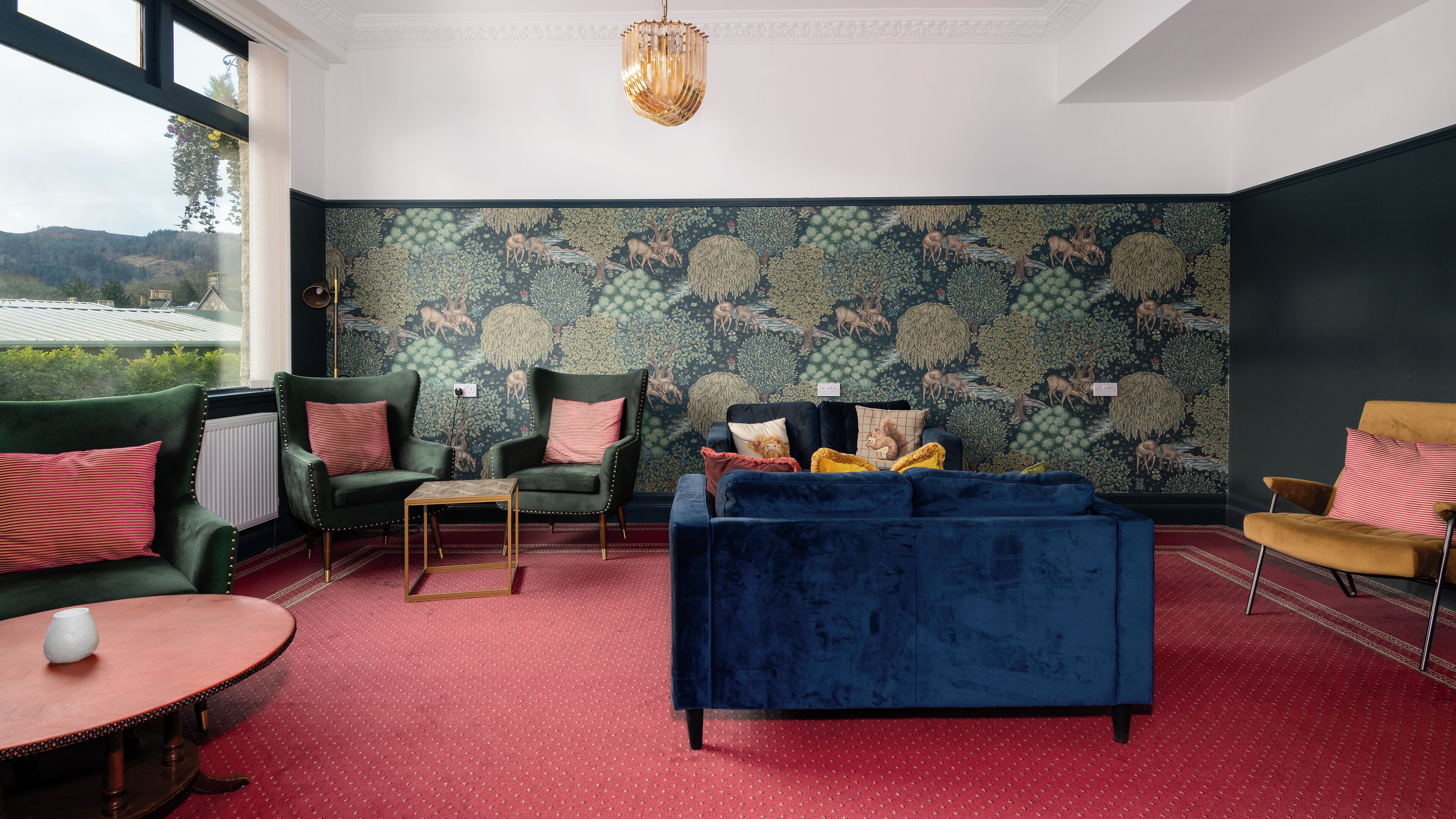 Een kamer met een groene bank, een blauwe bank en twee fauteuils met rode en roze kussens. Een gouden kroonluchter hangt aan het plafond.
