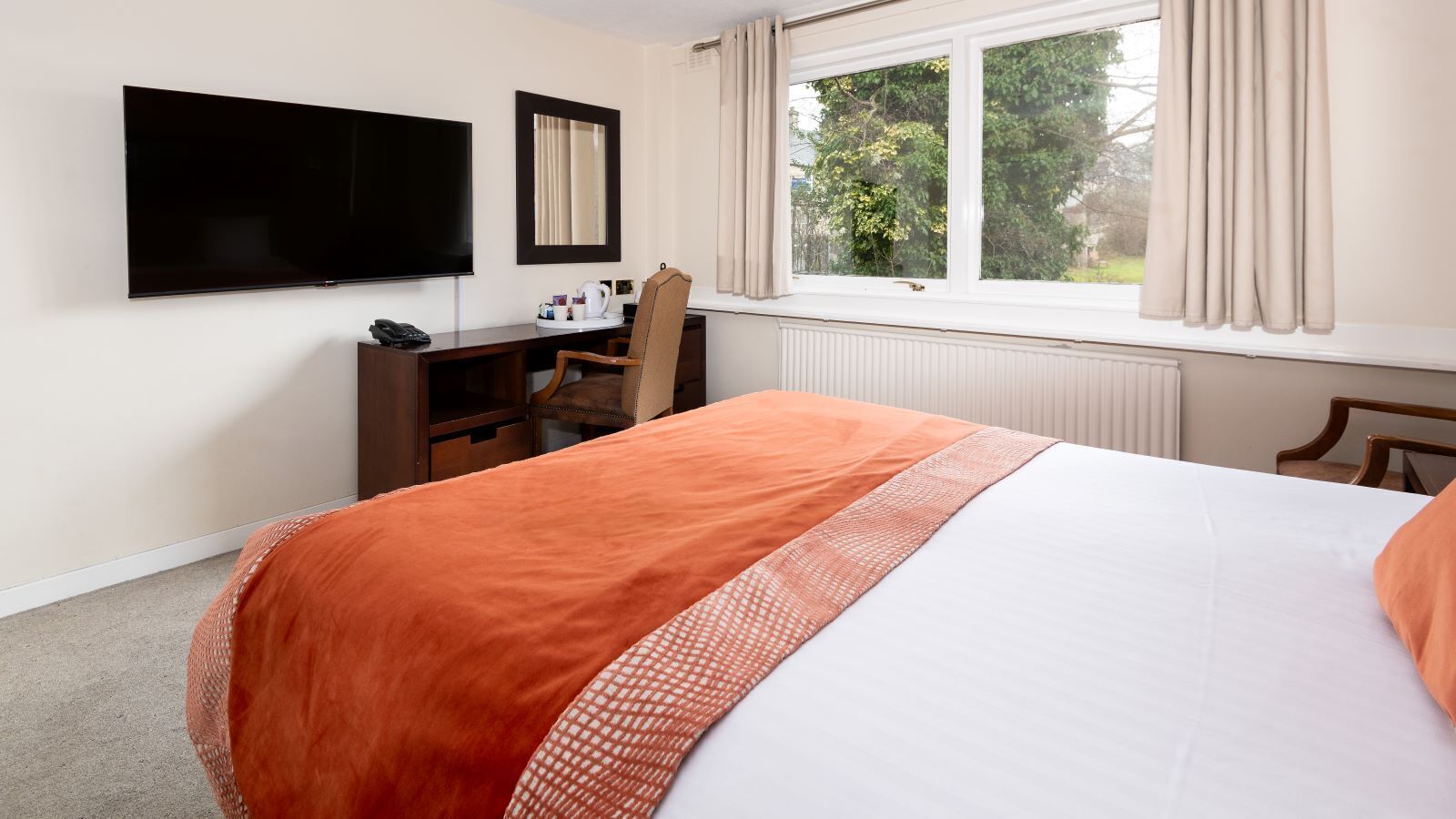 A hotel room with a bed, a desk, a chair, a TV, and a window with curtains.