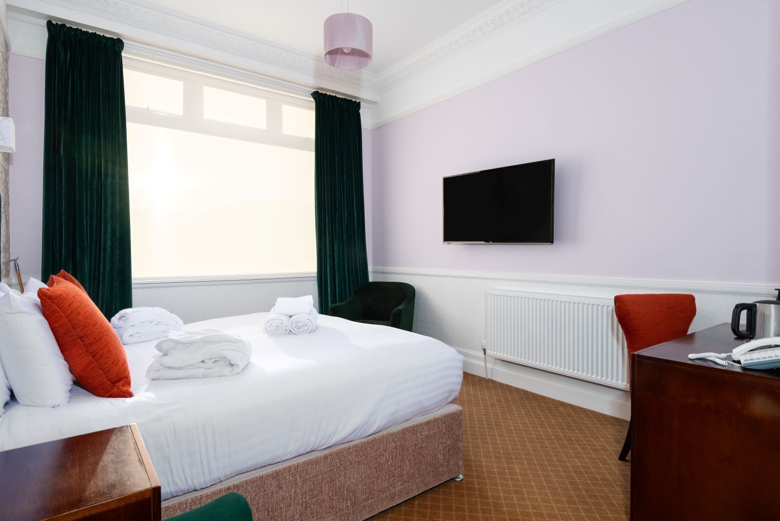 A hotel room with a bed, a desk, a chair, a television, and a window with curtains.
