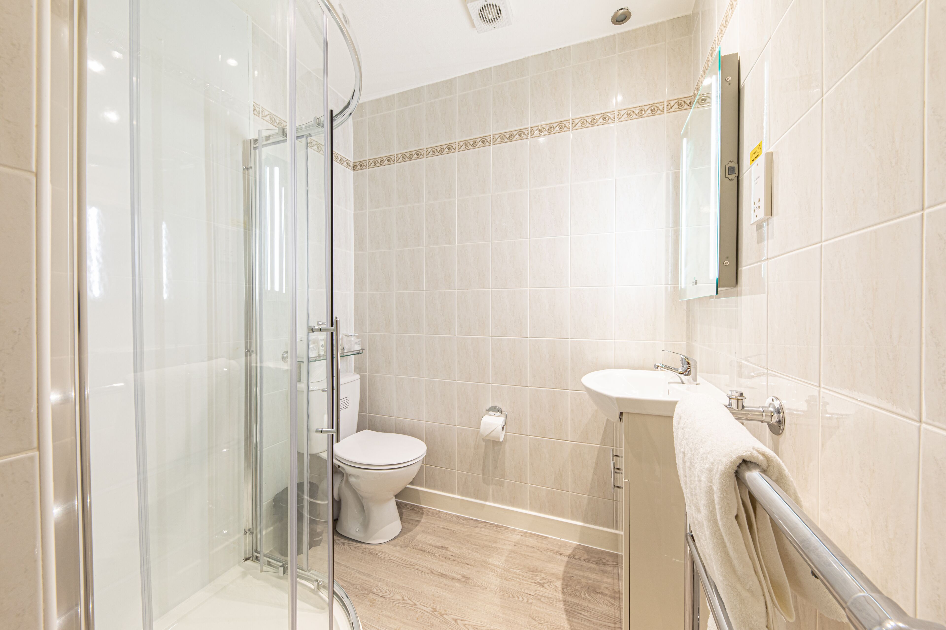 Ein modernes Badezimmer mit Duschkabine aus Glas, Toilette und Waschbecken mit Handtuchhalter.