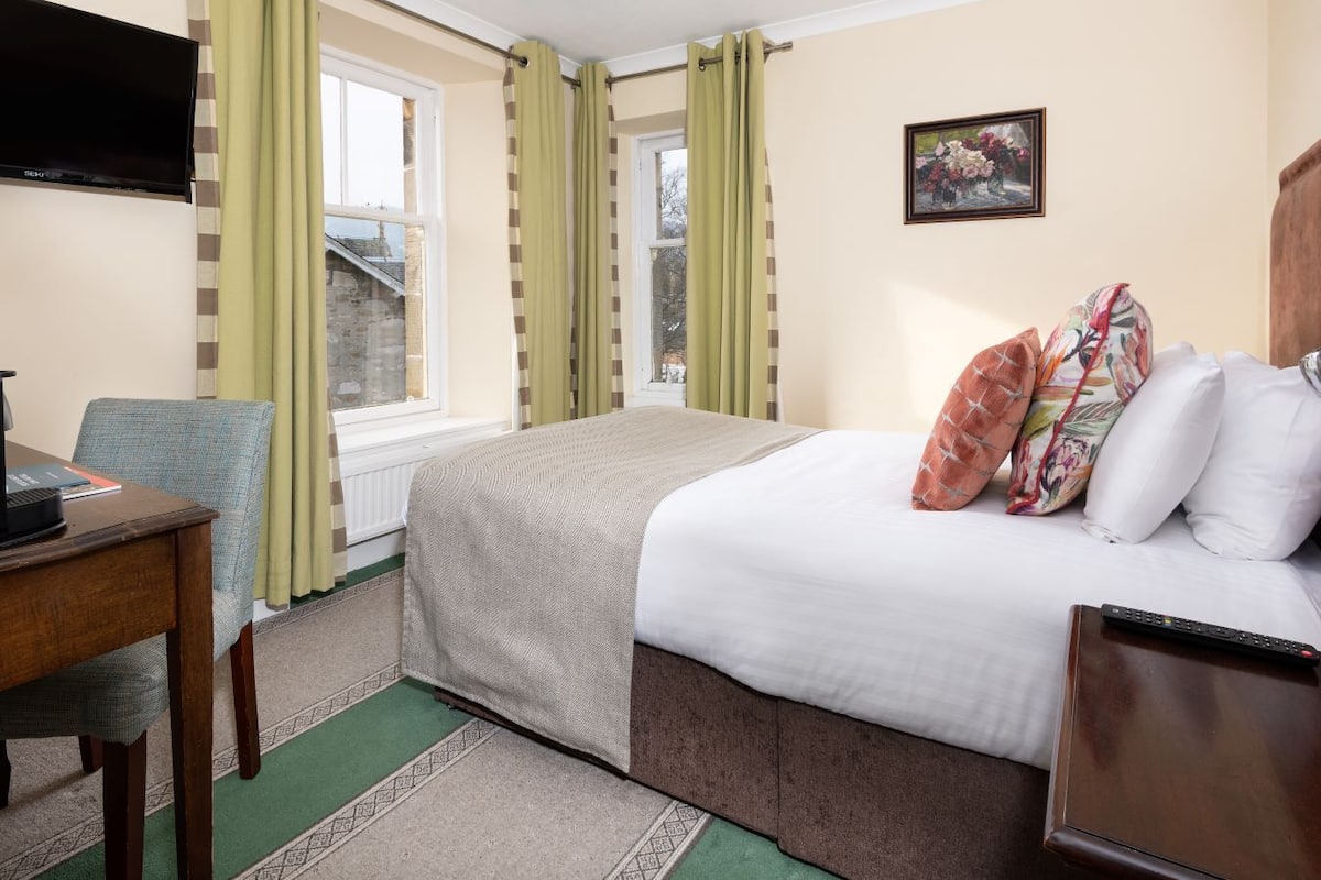 A hotel room with a bed, a desk with a laptop, a television, and a window with curtains.