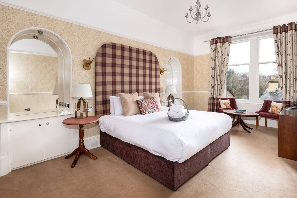 A hotel room with a large bed, a bedside table, a chair, a desk, and a window with curtains.