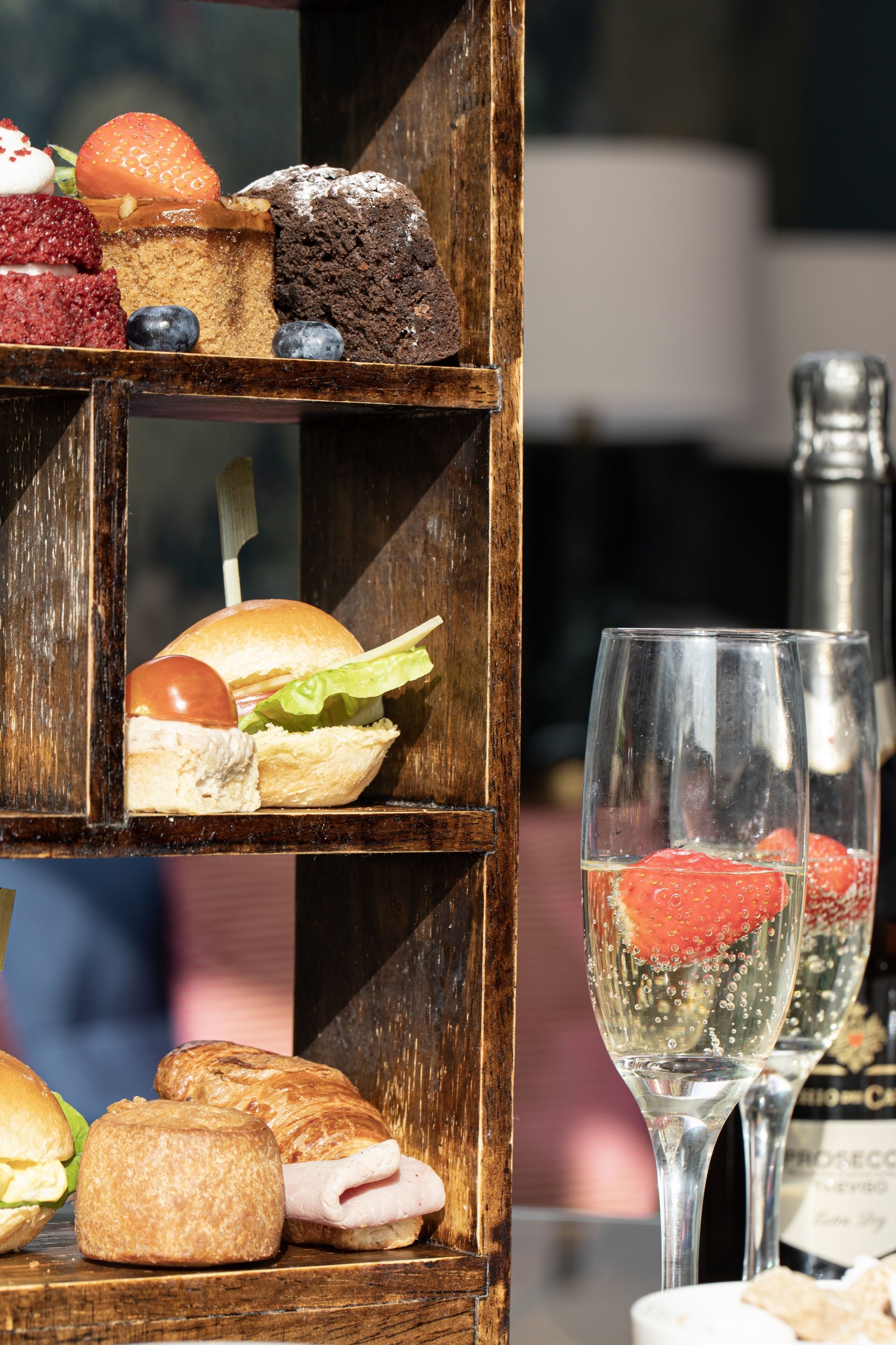 A wooden display case with various pastries and sandwiches, and two glasses of champagne.