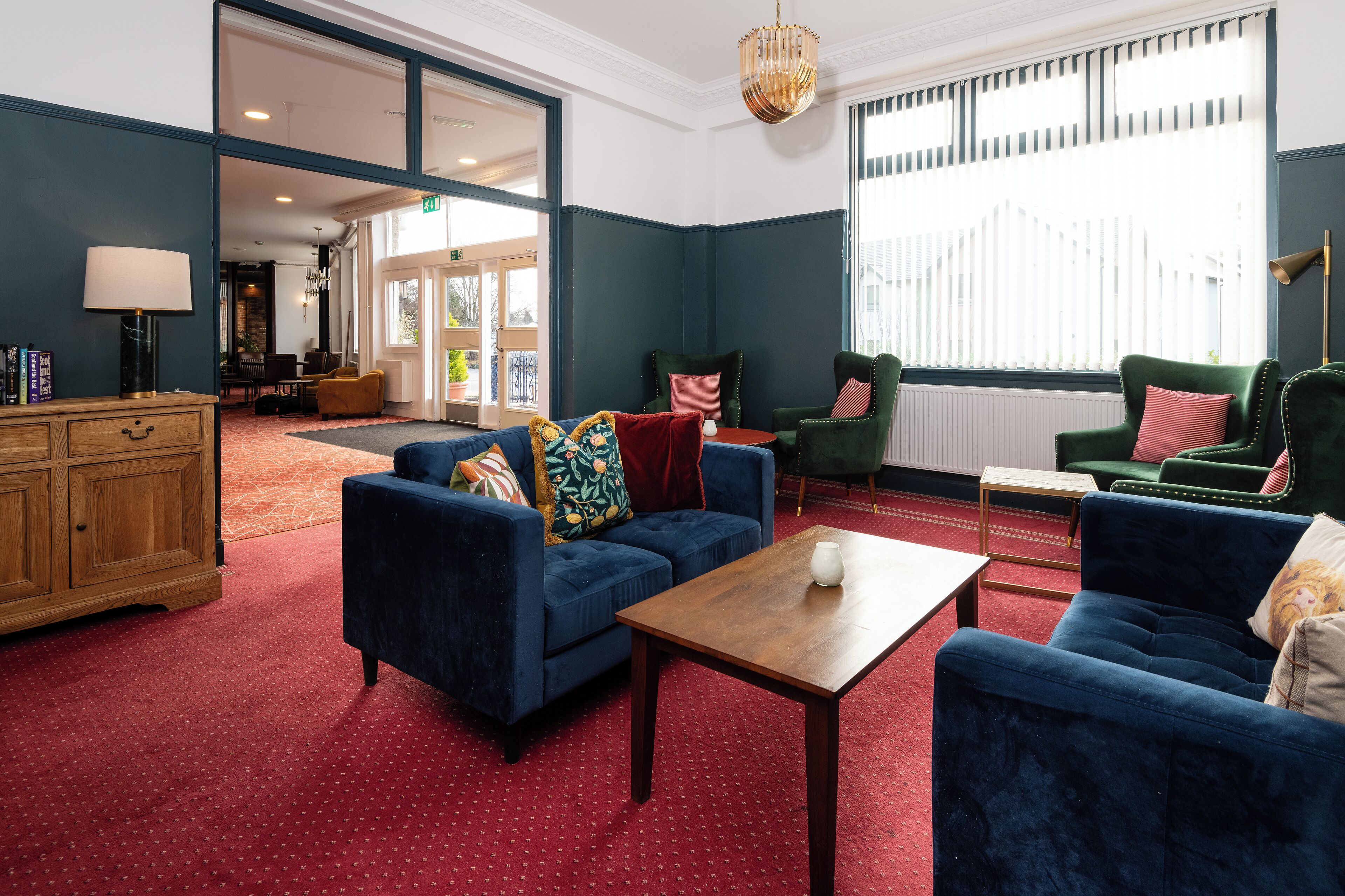 A spacious lobby with a blue sofa set, a wooden cabinet, and a red carpeted floor.