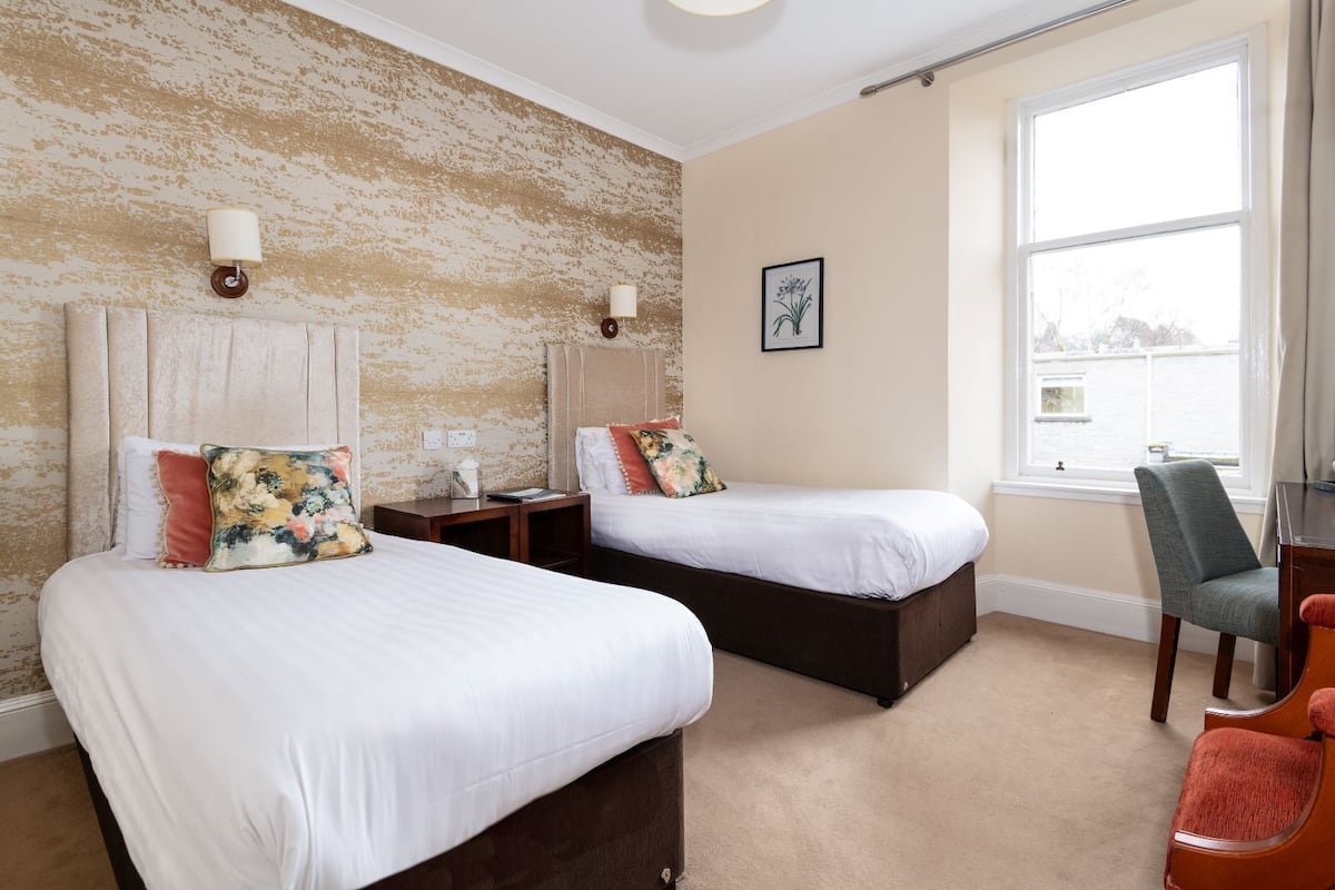 A hotel room with two beds, a chair, a desk, and a window with a view.