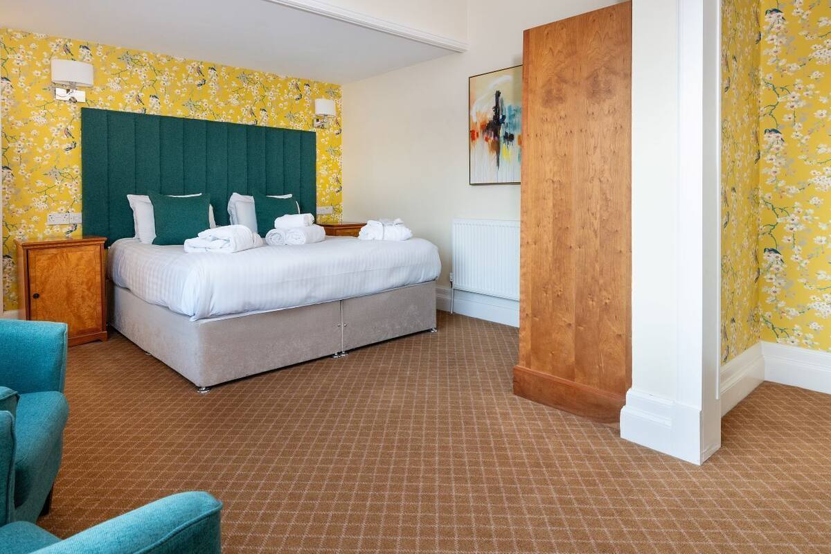 A hotel room with a bed, a blue armchair, and floral wallpaper.