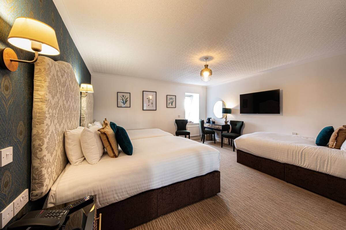 A hotel room with two beds, a desk, a chair, a TV, and a lamp.