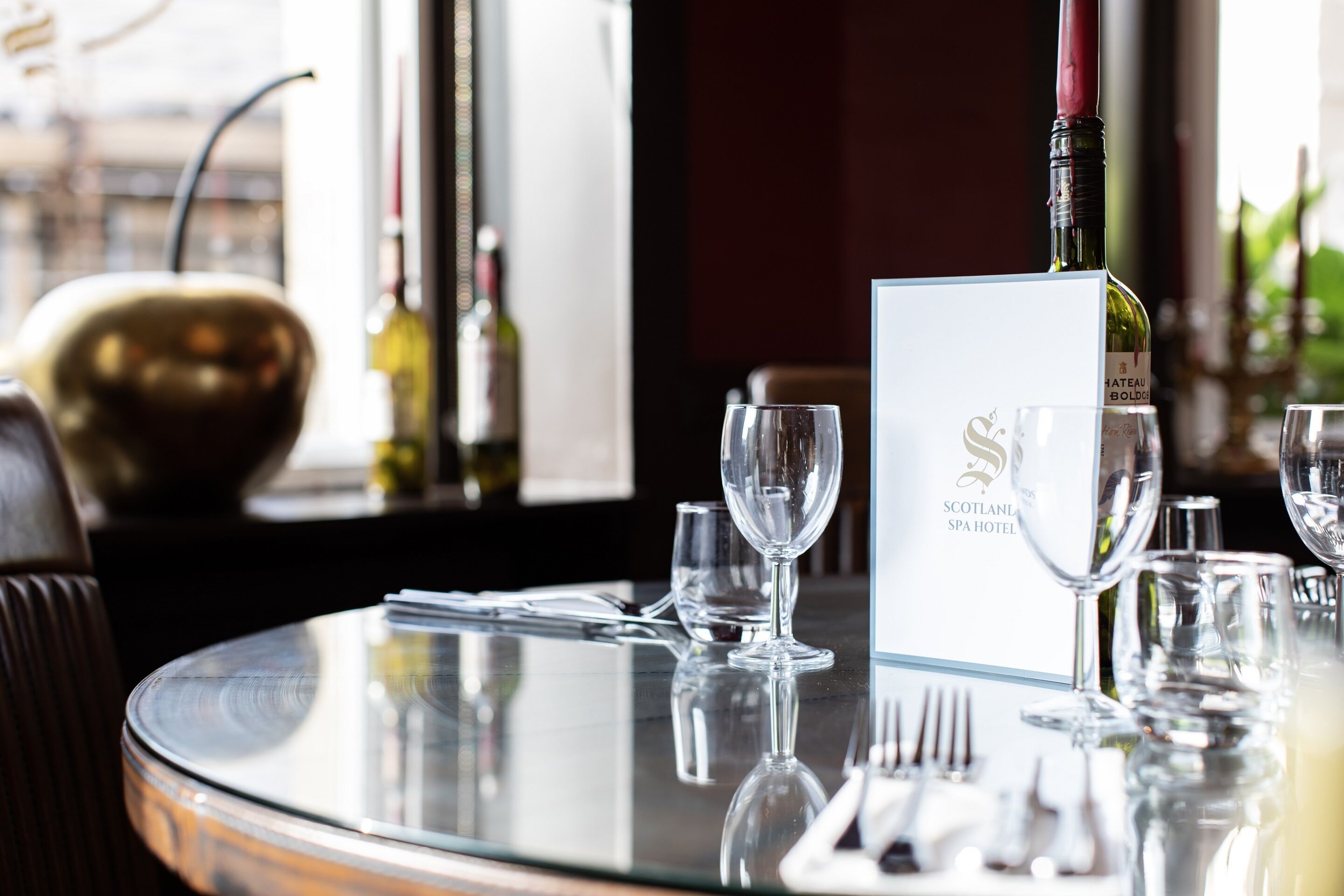 Una mesa redonda de cristal con un atril para menú, una botella de vino y copas de vino vacías.