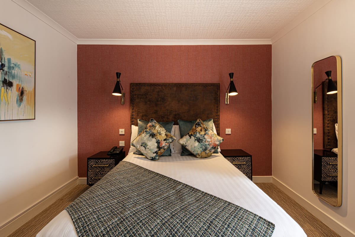 A hotel room with a large bed, two nightstands, a mirror, and a painting on the wall.
