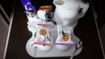 Una máquina de café blanca con un botón rojo, dos paquetes de galletas Shortie Squirrel de Meredith Drew y un paquete púrpura de chocolate Cadbury Dairy Milk.