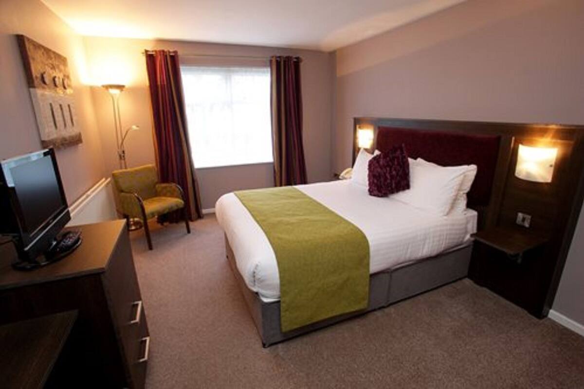 A hotel room with a bed, a desk with a TV, a chair, and a window with curtains.