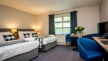 A hotel room with a bed, bedside tables, a desk, a chair, a TV, and a window with curtains.