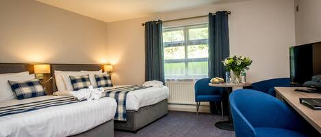 A hotel room with a bed, bedside tables, a desk, a chair, a TV, and a window with curtains.