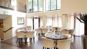 A spacious dining area with multiple round tables and chairs, large windows, and a staircase leading to an upper level. - Waterfoot Hotel (Londonderry)