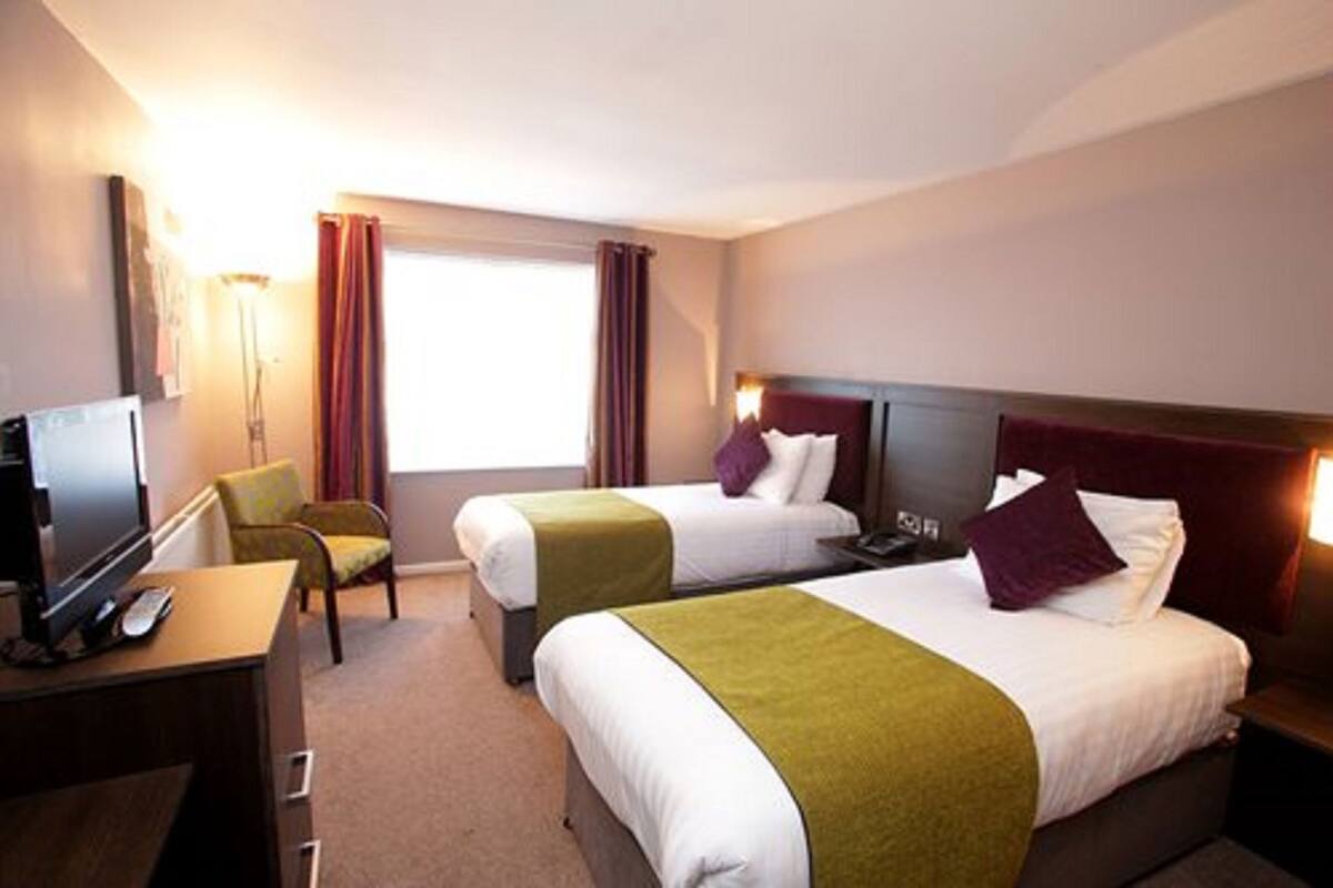 A hotel room with two beds, a desk with a TV, and a chair.