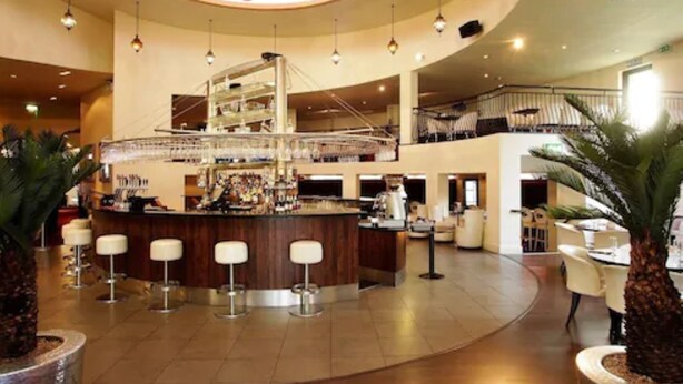 A spacious lobby with a central bar area, multiple seating arrangements, and a staircase leading to an upper level. - Waterfoot Hotel (Londonderry)